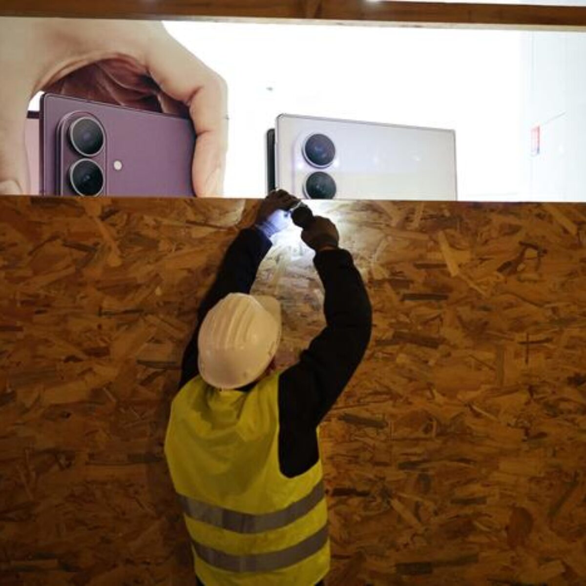 A worker installs a wooden panel to board up the shop window of the Samsung store ahead of a demonstration planned for October 24, Boulevard Malesherbes in central Paris on October 23, 2026, following last weekend's demonstrations that degenerated into the worst street violence in years. France will deploy some 70,000 security personnel nationwide for new protests this weekend, Interior Minister said on October 23, warning that calls for violence and looting were already circulating on social media. (Photo by SIMON WOHLFAHRT / AFP)